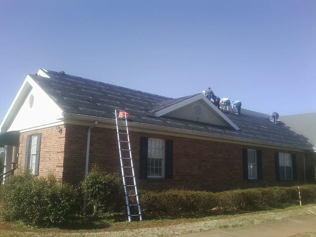 Crew tearing shingles off a brick ranch roof with a ladder set — Emergency Roof Repair work by our crew in Avon